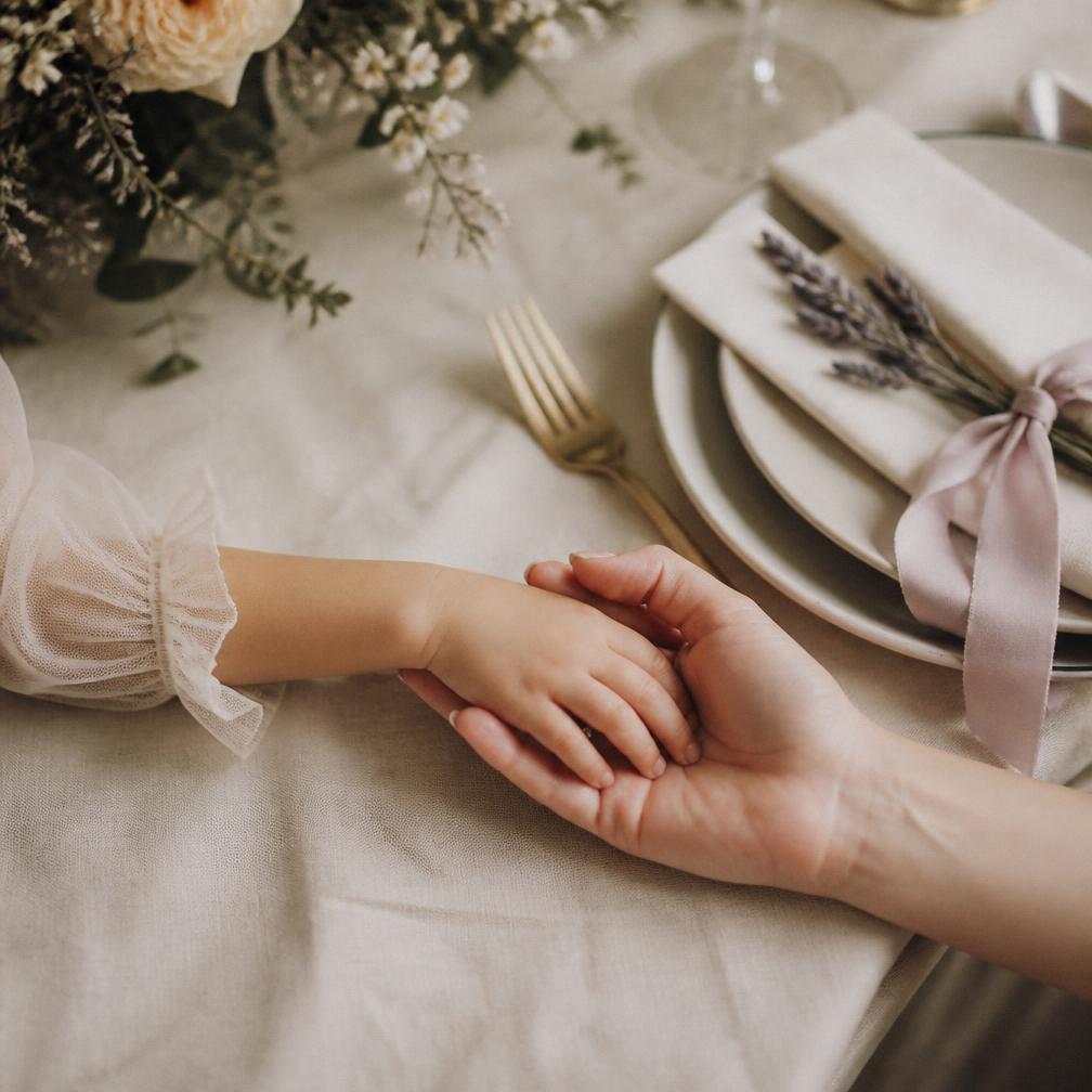 A child's hand resting in her mother's at a wedding table